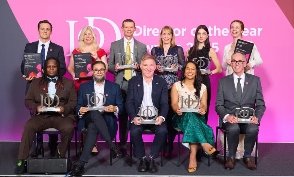 Ten people in formal attire sit and stand holding awards, smiling in front of a pink "Director of the Year" backdrop. - Home Instead