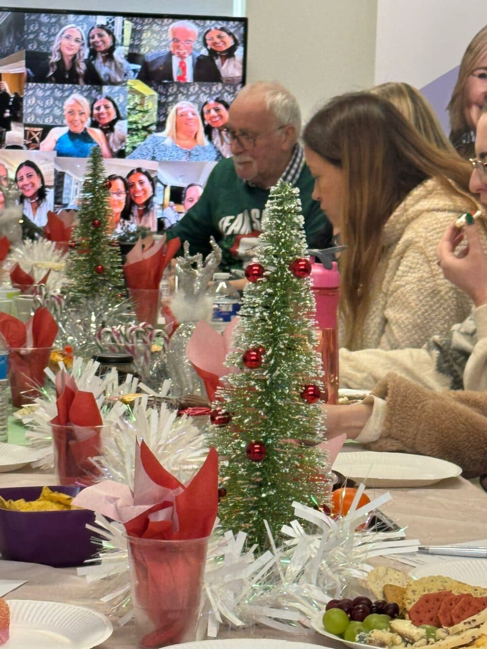 People enjoy a festive holiday meal with Christmas decorations; others join via video call in the background. - Home Instead