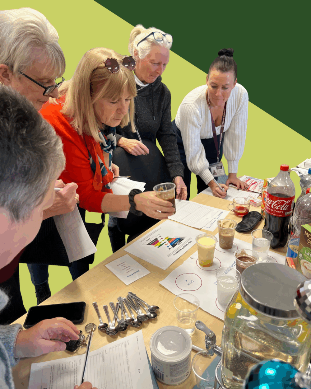 Five women gather around a table, examining drinks and papers during a tasting or experiment activity. - Home Instead