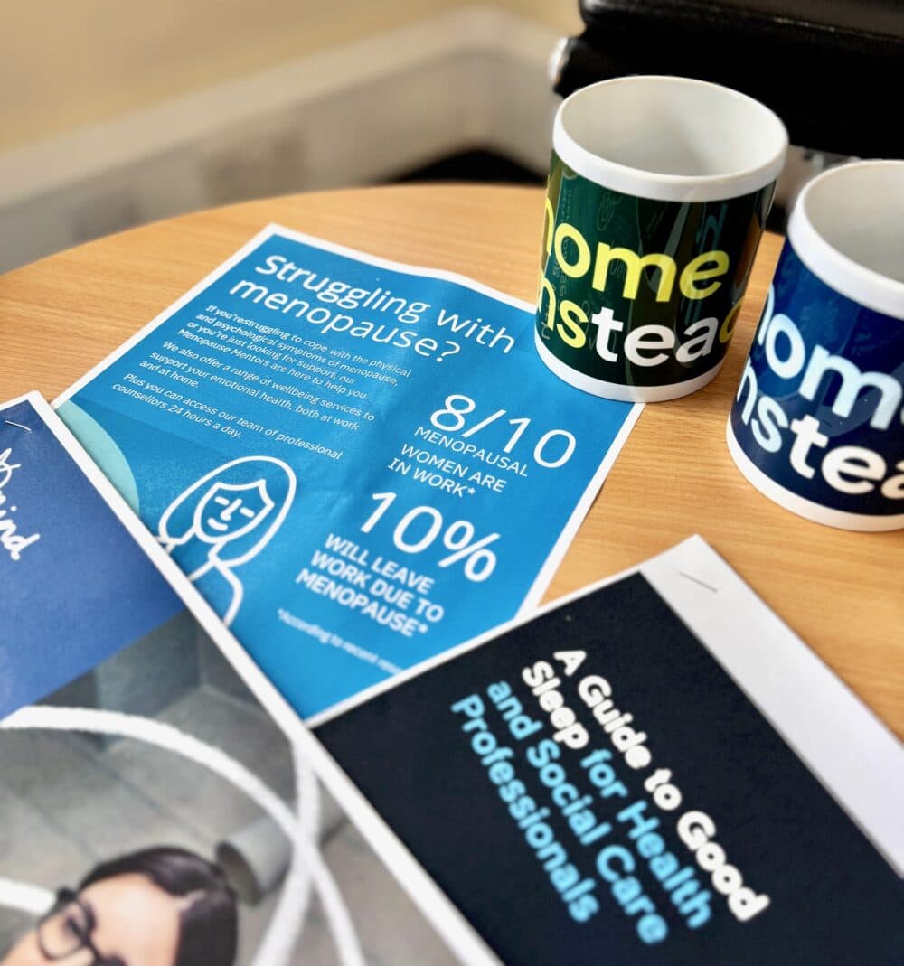 A table with menopause information leaflets and two mugs, one reading "home instead", on top. - Home Instead