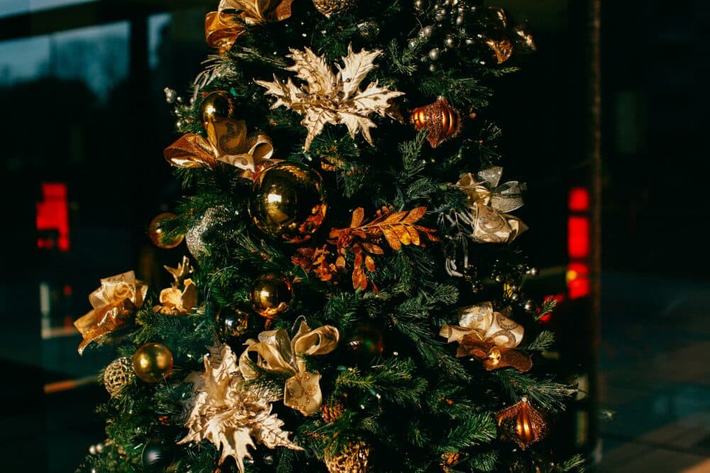 A Christmas tree decorated with gold and bronze ornaments and ribbons. - Home Instead