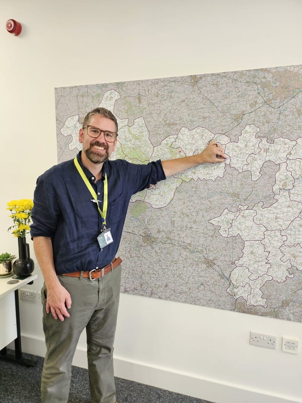 Smiling man points at a location on a large map on the wall in an office setting. - Home Instead