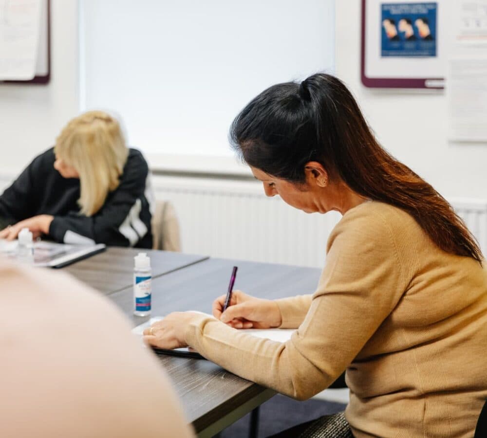 A woman with long black hair writing on the desk