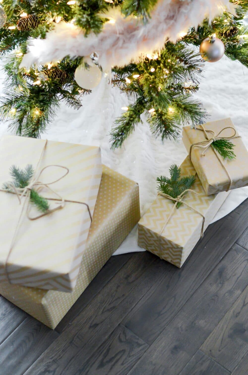 Wrapped presents with string and greenery sit under a decorated Christmas tree on a wooden floor. - Home Instead