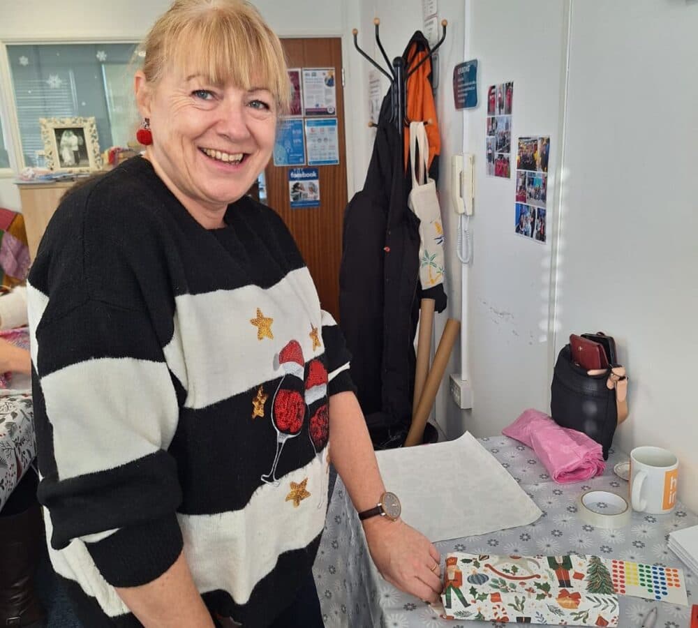 A woman with blonde hair wearing black and white stripes wrapping a gift while standing happy and smiling