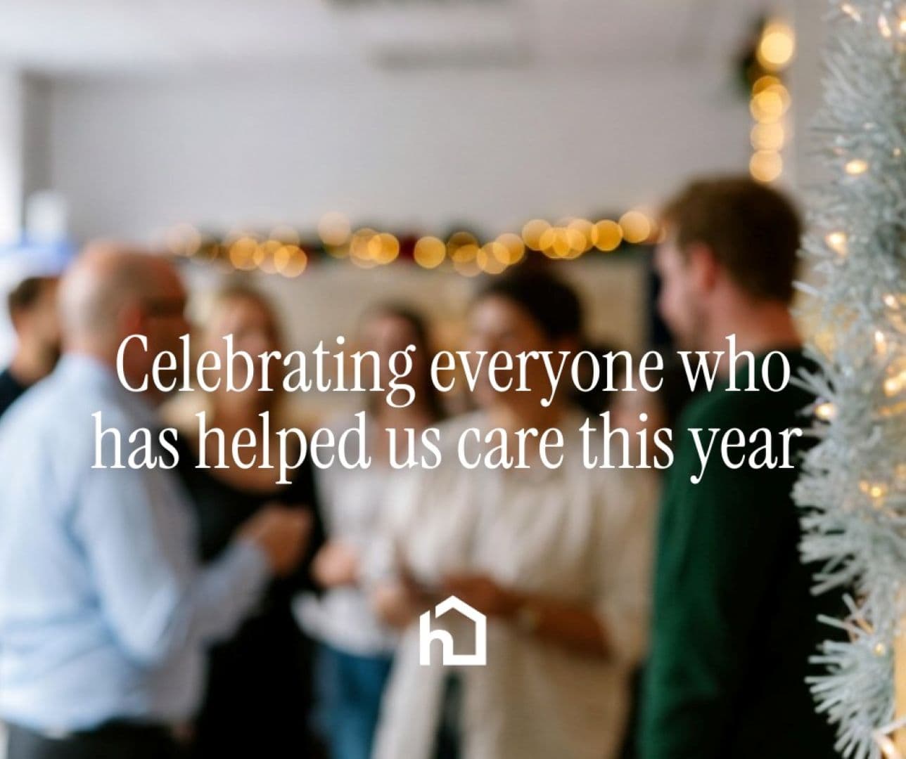 A group of people talking at a festive gathering with holiday lights and a decorated tree in the foreground. - Home Instead