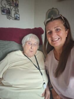 Elderly woman and middle-aged woman smiling together in a cosy living room. - Home Instead
