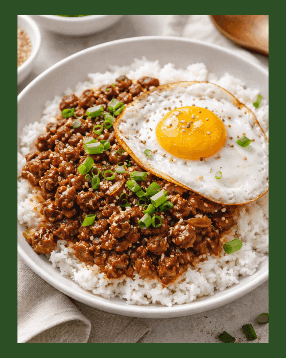 A bowl of rice topped with seasoned minced meat, a fried egg, and chopped spring onions. - Home Instead