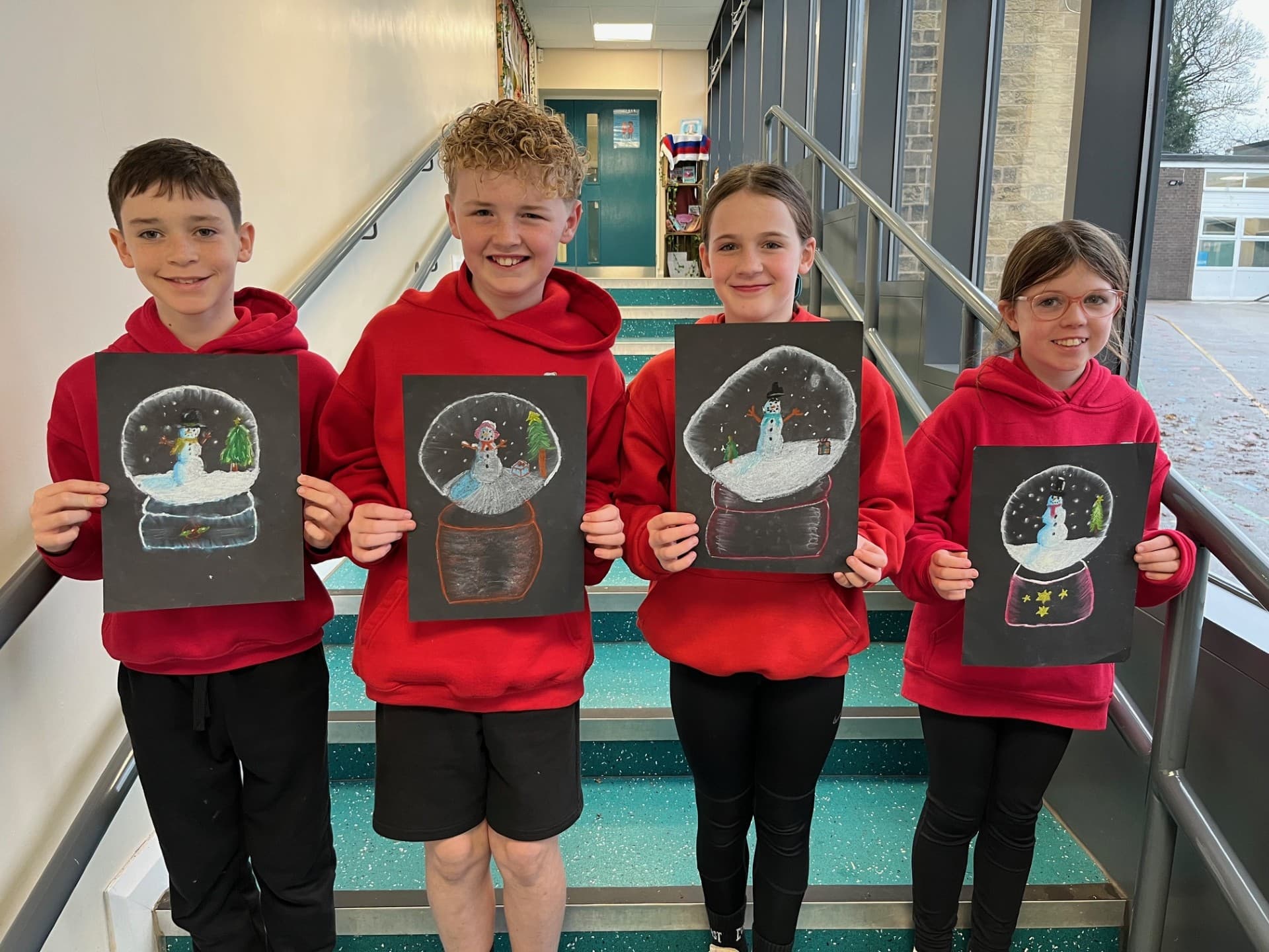 Four children in red hoodies hold up their snow globe drawings whilst standing on school stairs. - Home Instead