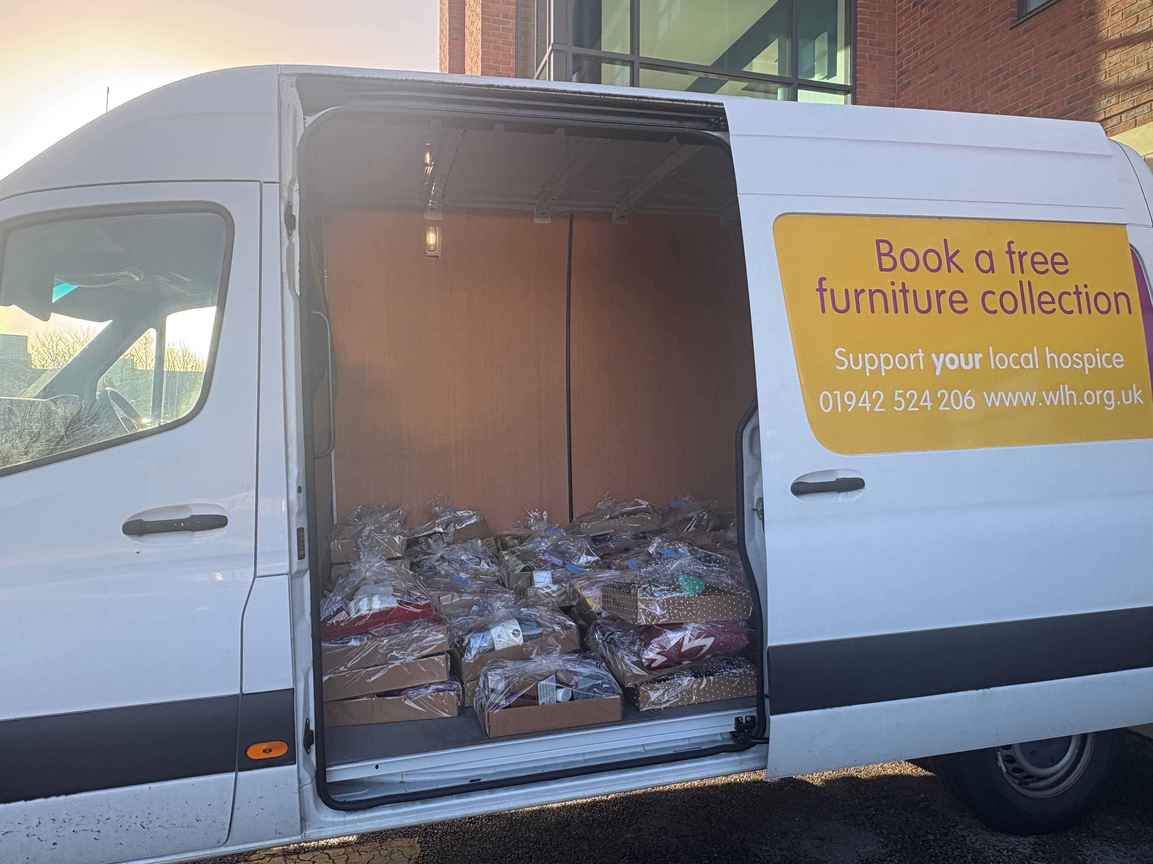 A van with its side door open, filled with packed items and a sign offering free furniture collection. - Home Instead
