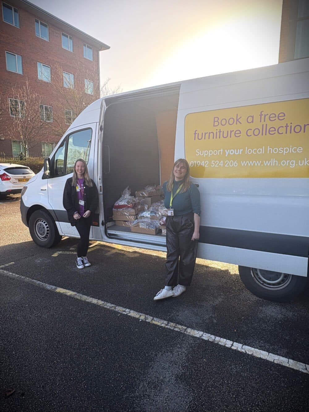Two women stand by a van with its side door open, showing bags inside. The van advertises furniture collection. - Home Instead