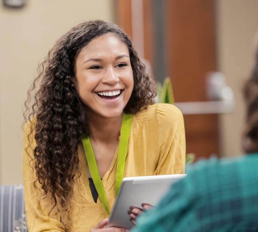 A woman with long curly hair happy and smiling while chatting with someone inside the room