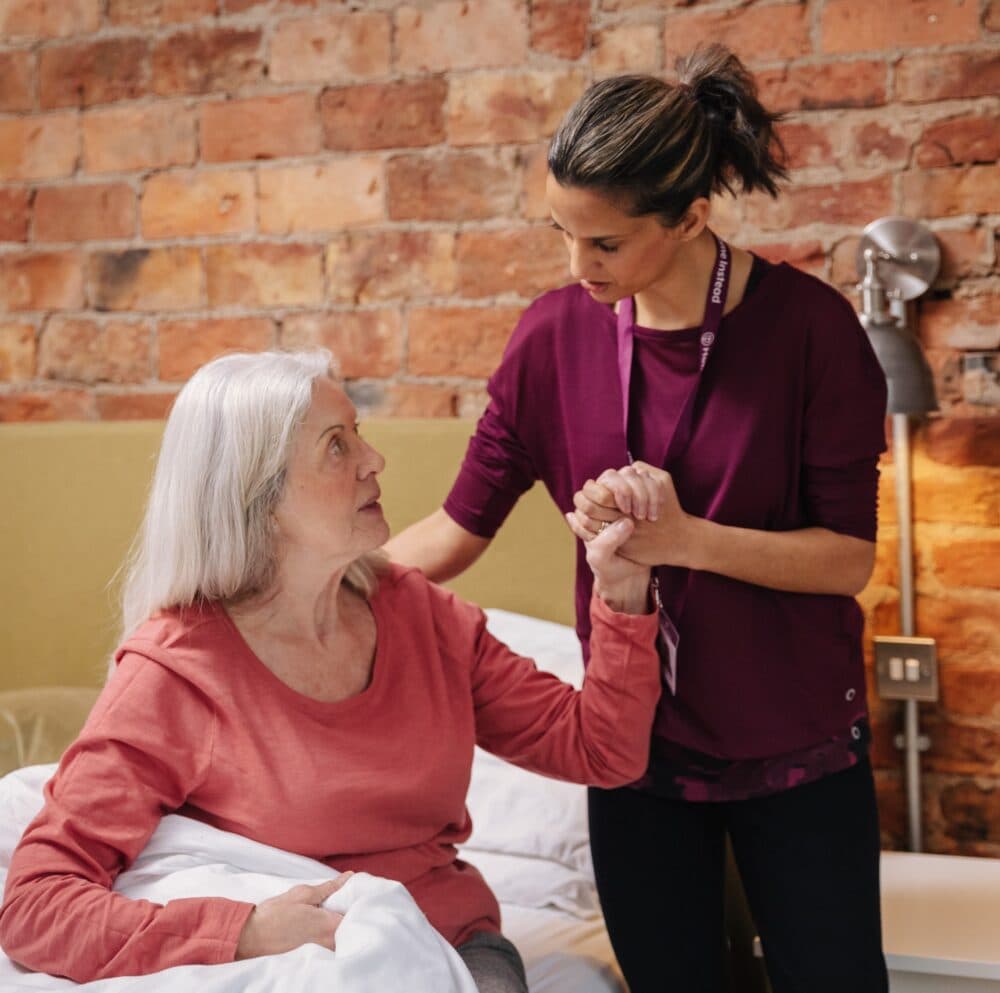 Female carer helping elderly woman to get up out of bed