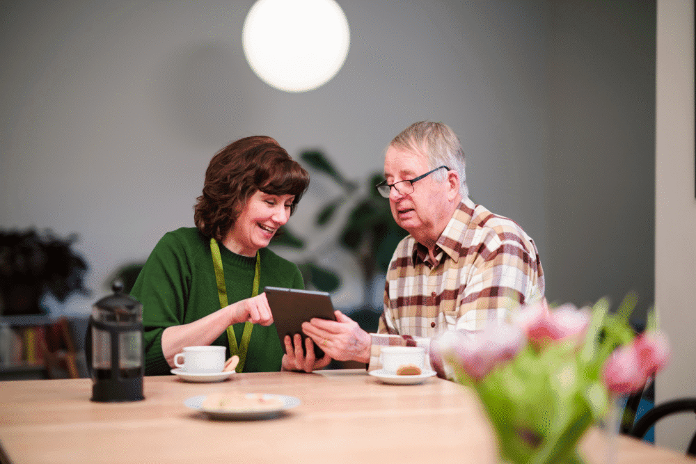 Home Instead Care Professional with a male elderly client holding a tablet gadget