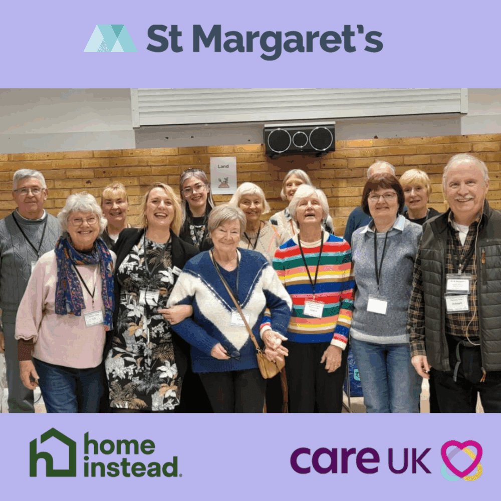 A group of smiling older adults pose together indoors, with logos for St Margaret’s, Home Instead, and Care UK. - Home Instead