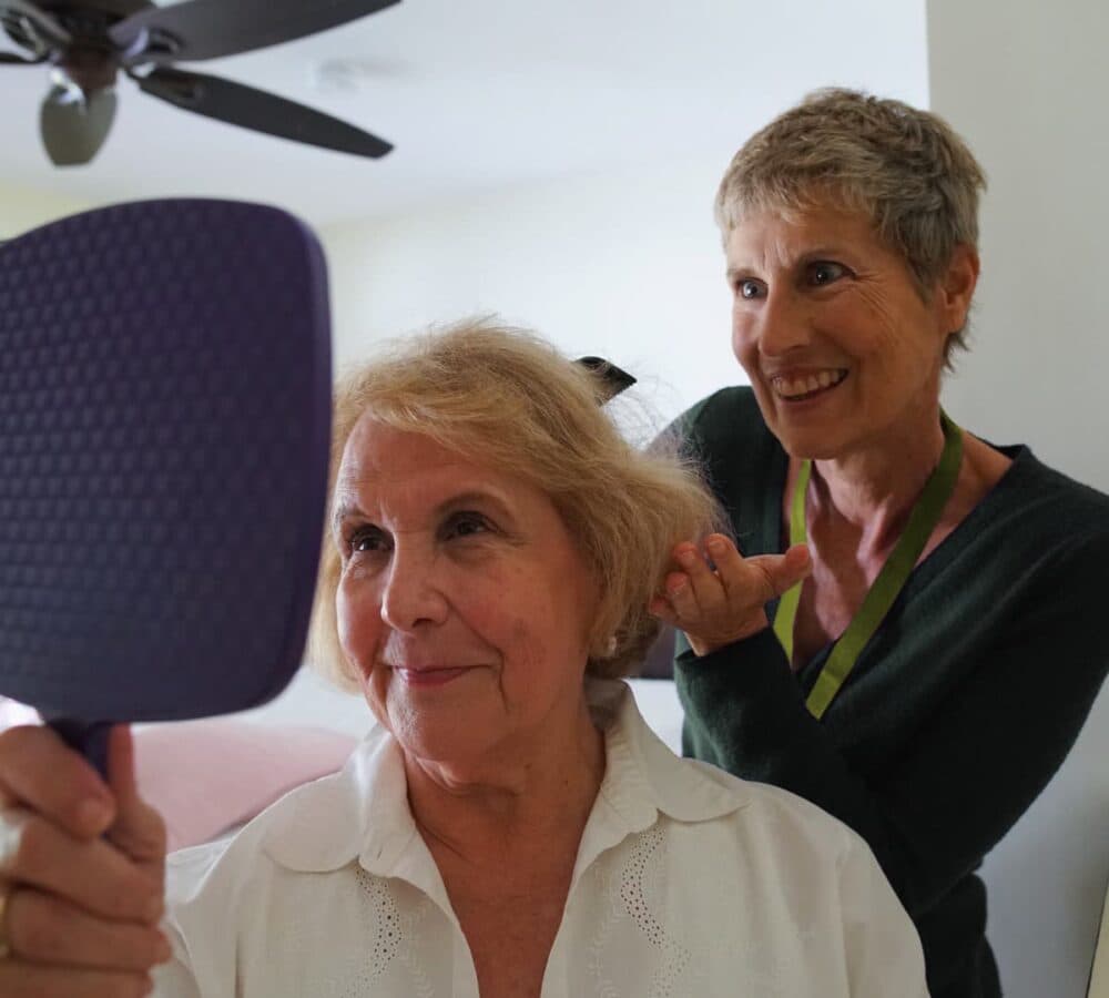 A female carer combing the hair of an older female adult while looking at the mirror