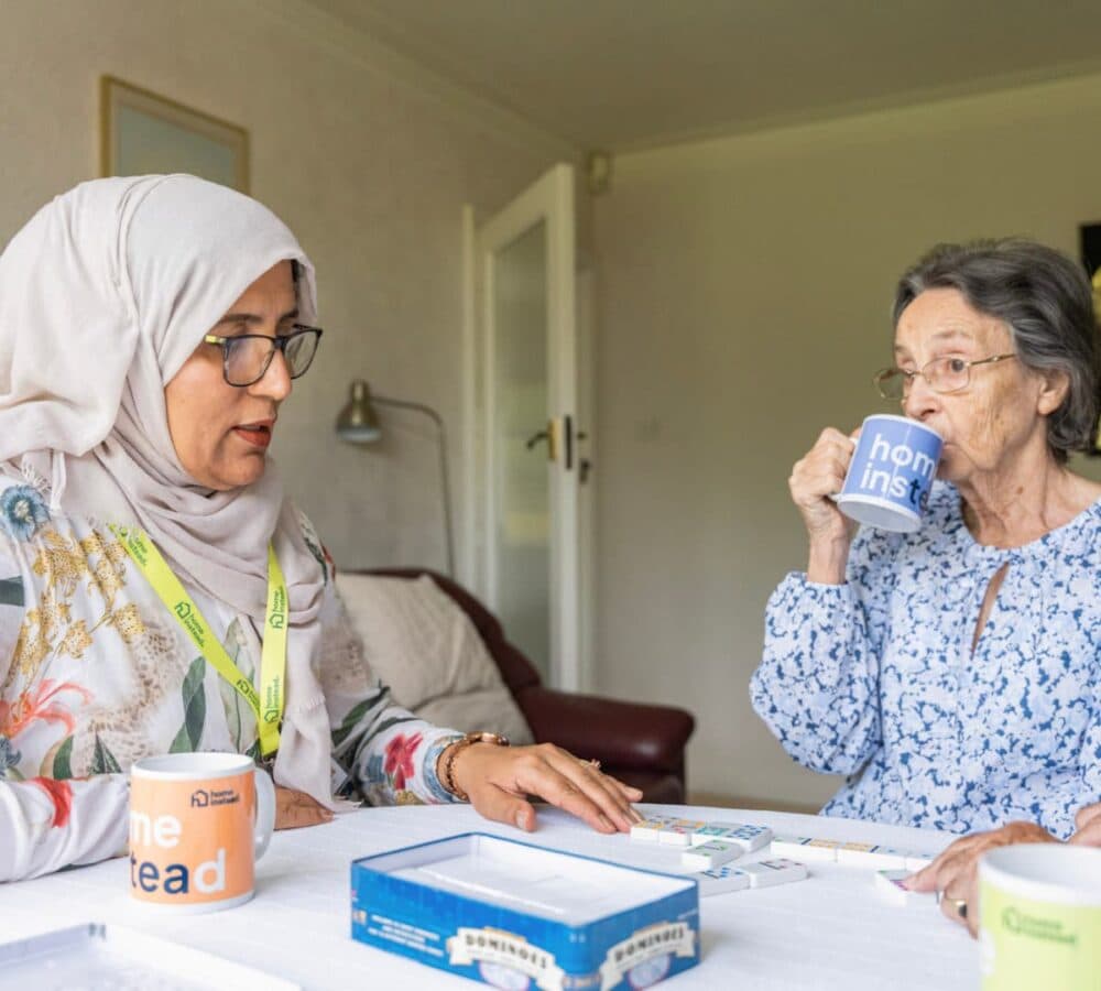 AN older female adult with short hair and sipping coffee while playing with her younger female carer inside the house