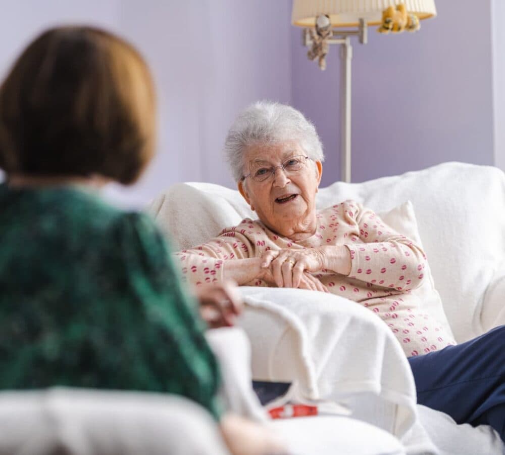An older female adult with grey hair happy and smiling while sitting on a white couch