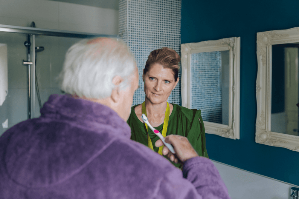 A Home Instead Care Professional helping an elderly male client brush his teeth