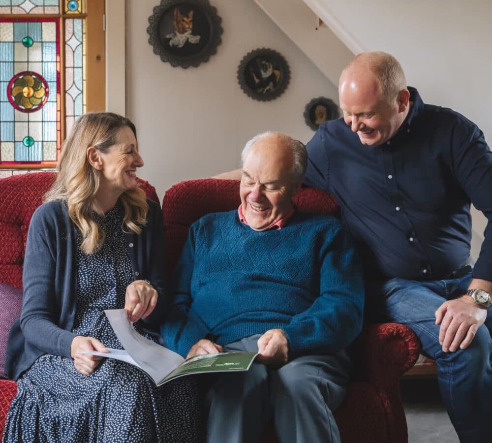 Three people wearing blue reading and happy and smiling while sitting on a red couch inside the house