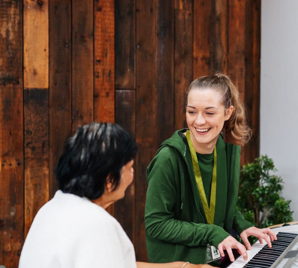A female with long hair happy and smiling while playing the piano and chatting with a female older adult