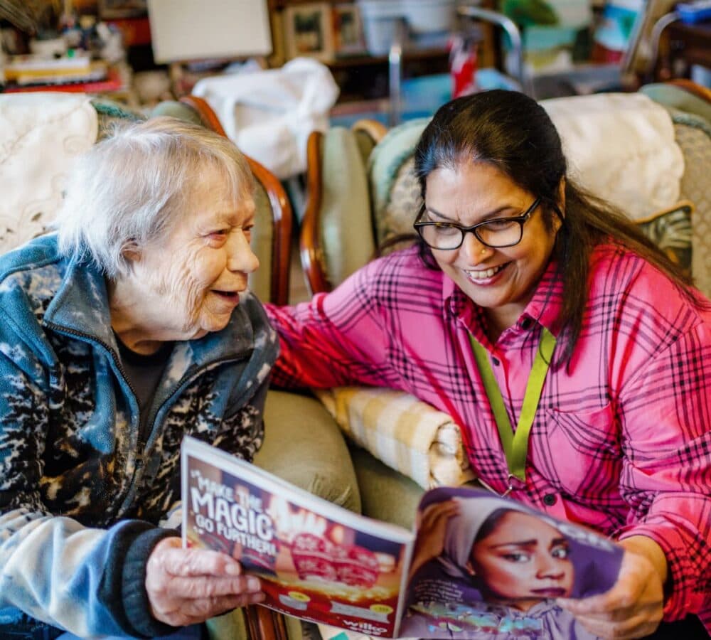 Two women chatting while reading together and sitting on the couch and happy and smiling