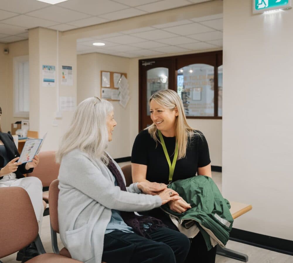 An older female adult with white hair chatting with her younger female carer with long blonde hair