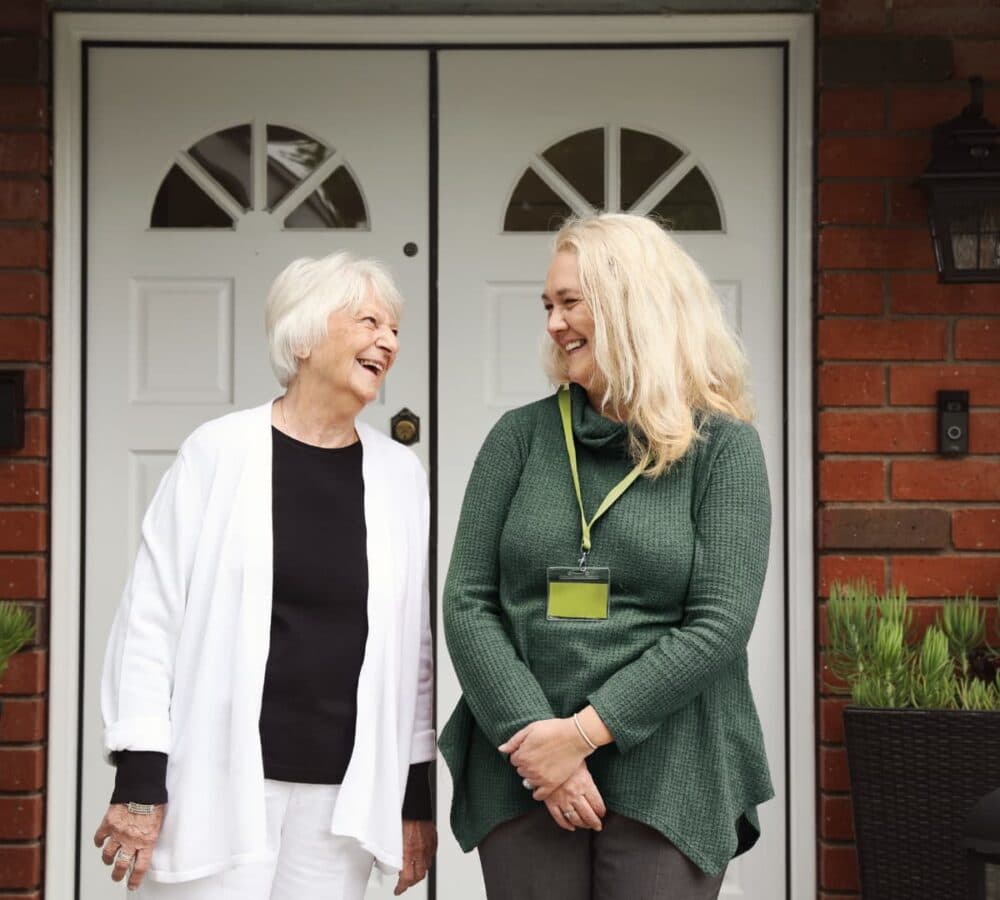 Two female happy and smiling while standing in front of the door of the house