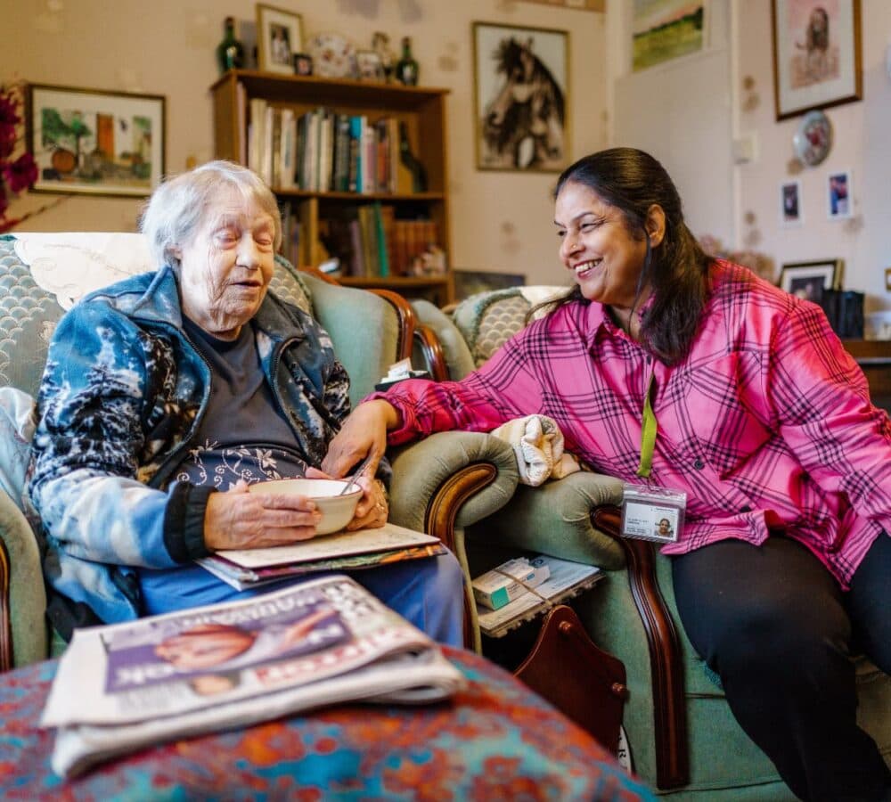 Two women chatting while sitting in teh couch inside the house
