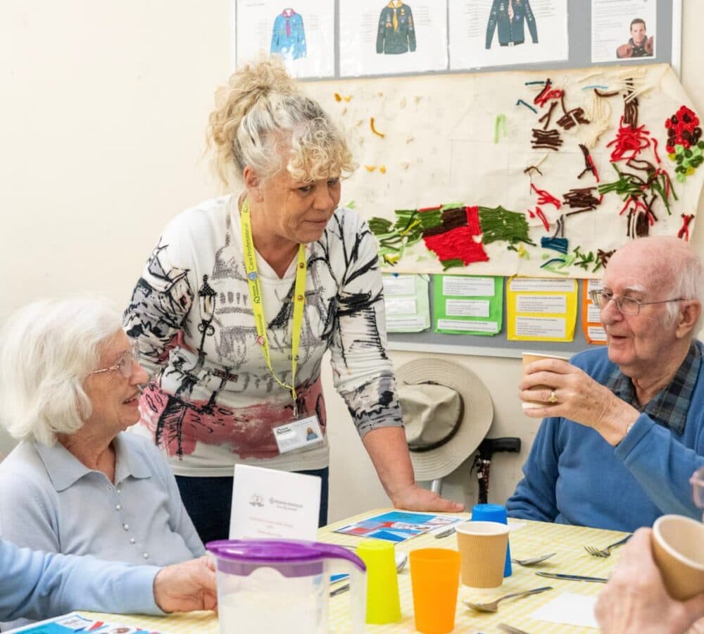 A female carer chatting with two older adults while sitting inside a room