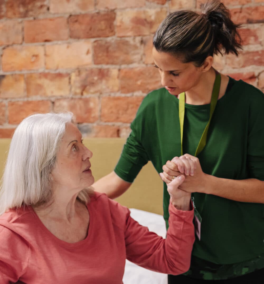 A carer helping and older lady out of her bed