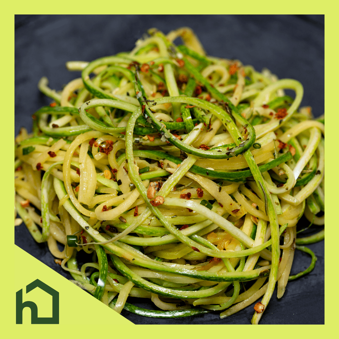 A photograph of a bowl of spaghetti with seems to be strands of courgette and chilli flakes in. The photo is surrounded by Home Instead branding with the logo in the bottom left corner
