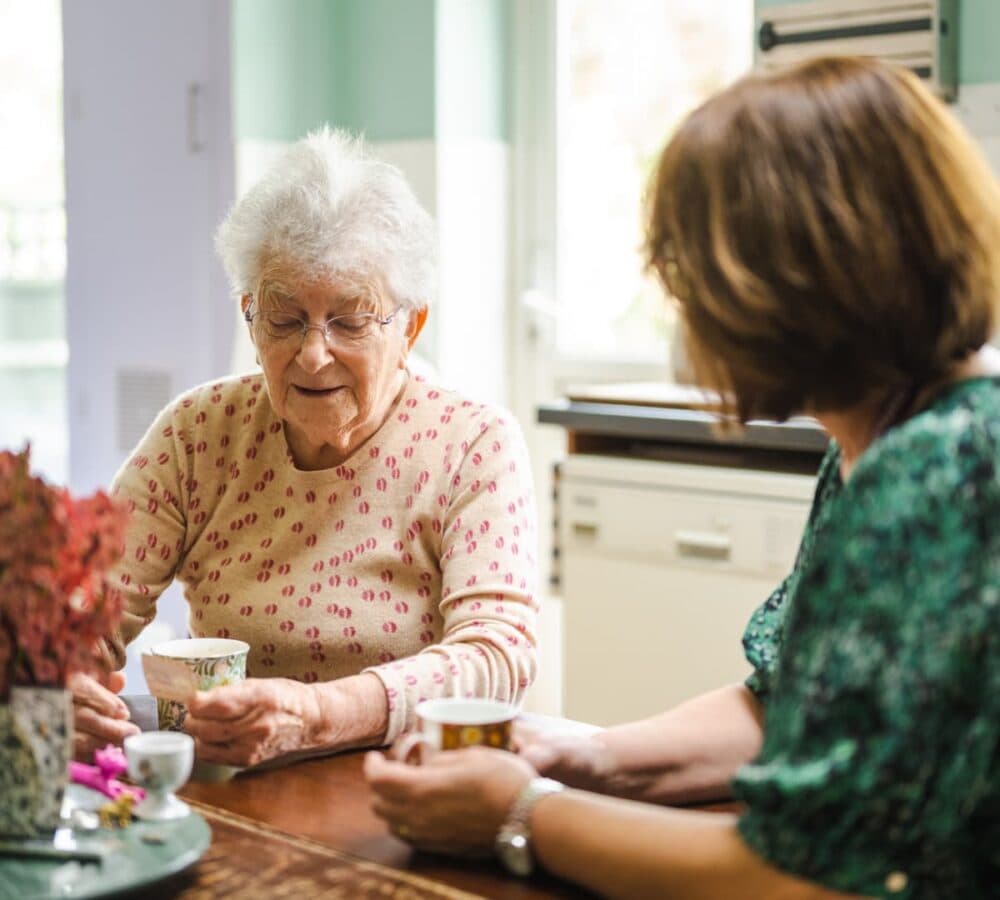 An older female adult with white hair chatting with her younger female adult inside the kitchen