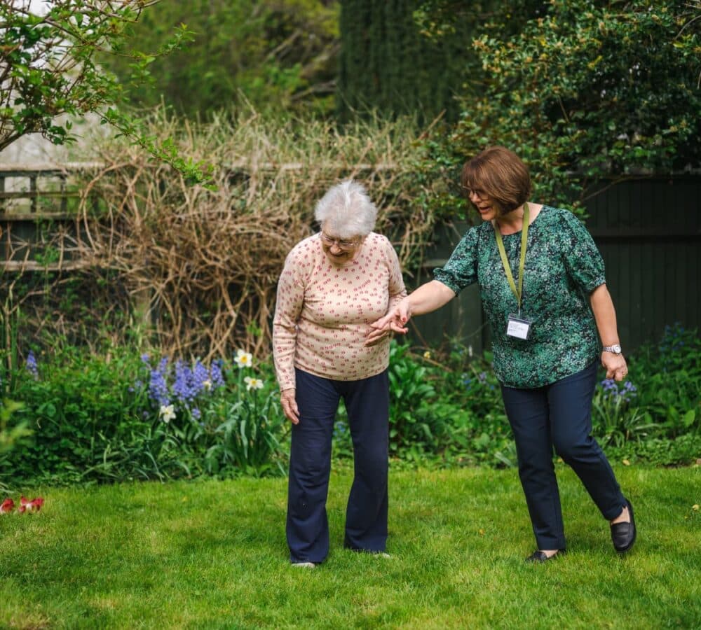 Two women smiling while walking in the garden with green grass