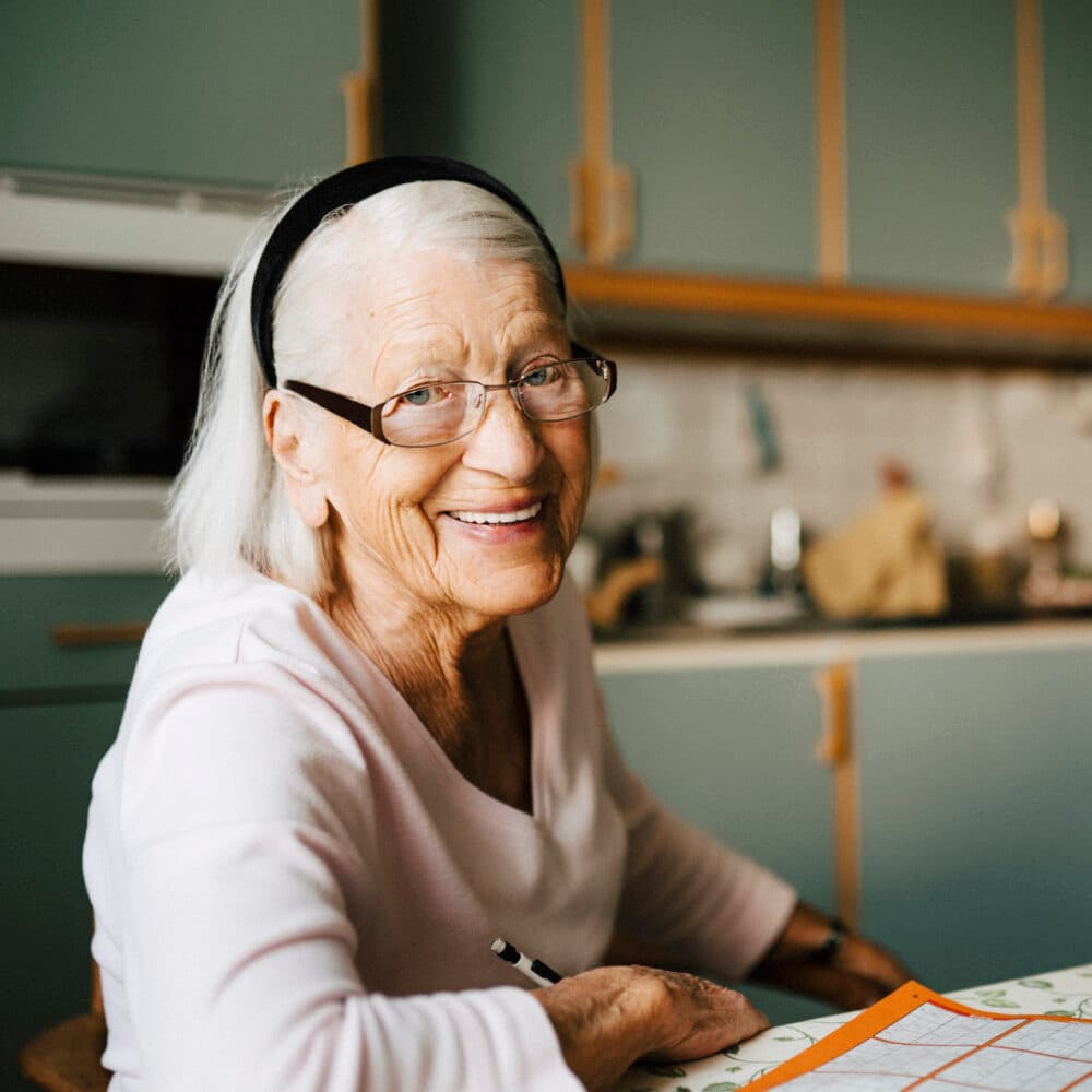 Portrait of smiling senior woman while male caregiver standing in background at home
