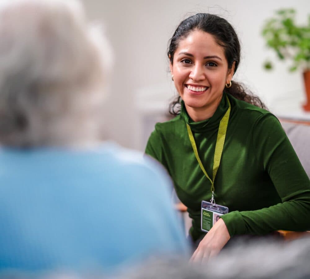 A woman with long black curly hair happy and smiling while sitting in the couch and chatting with an older woman