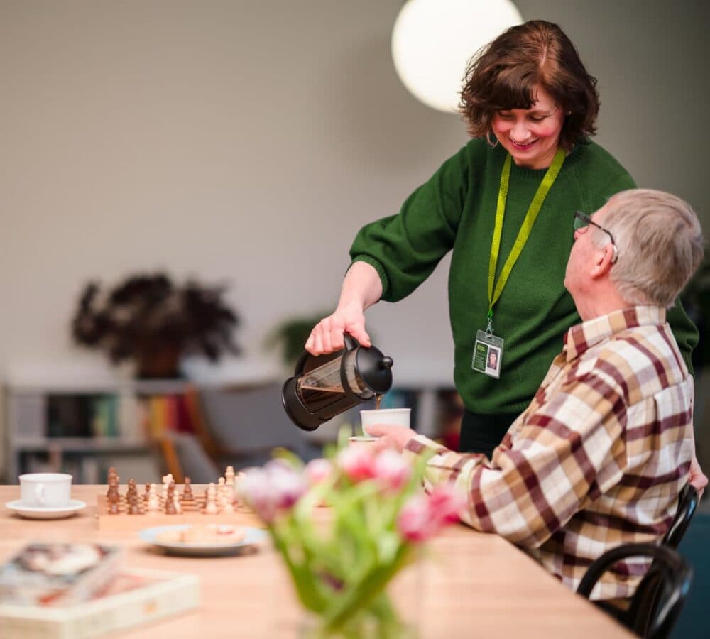 A younger woman pouring coffee on a cup with an olde rmale adult