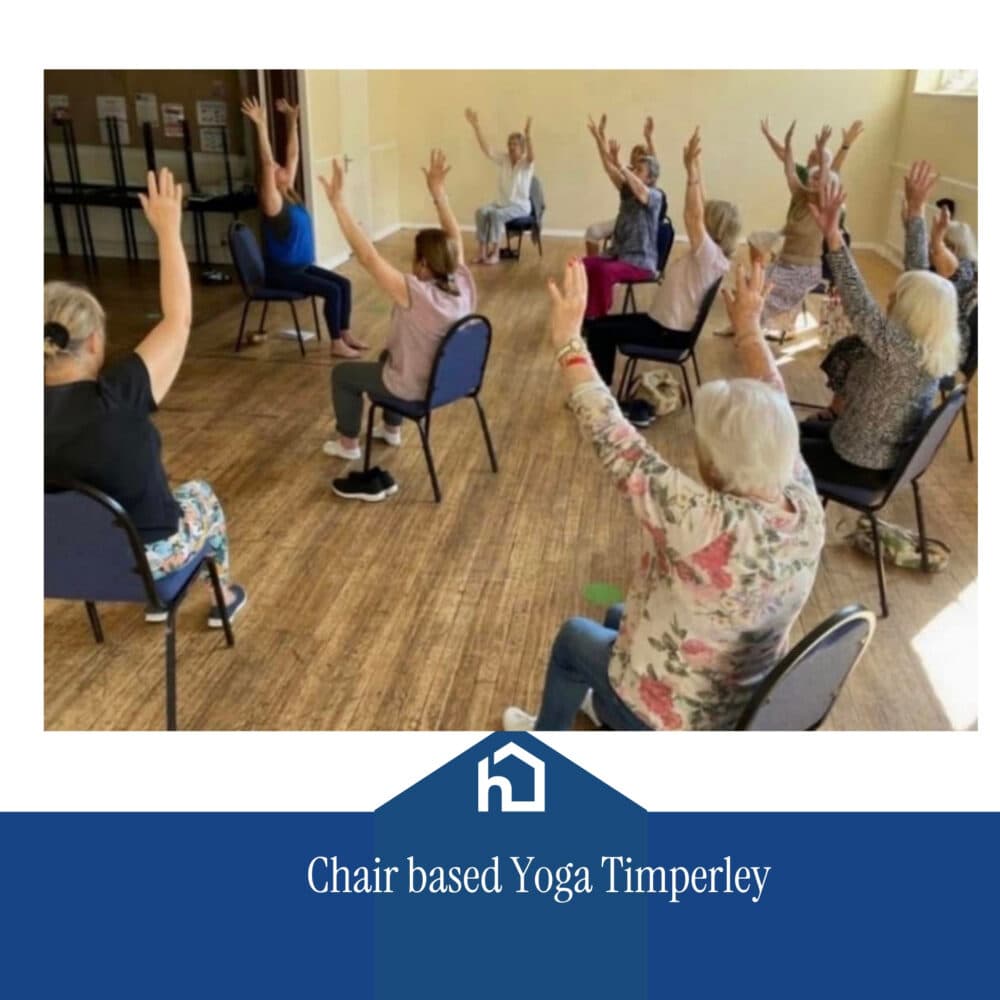 A group of people sit on chairs in a circle, raising their arms during a chair-based yoga class. - Home Instead