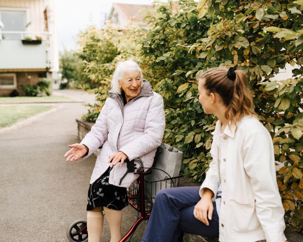 Smiling senior woman talking with female nurse at front yard