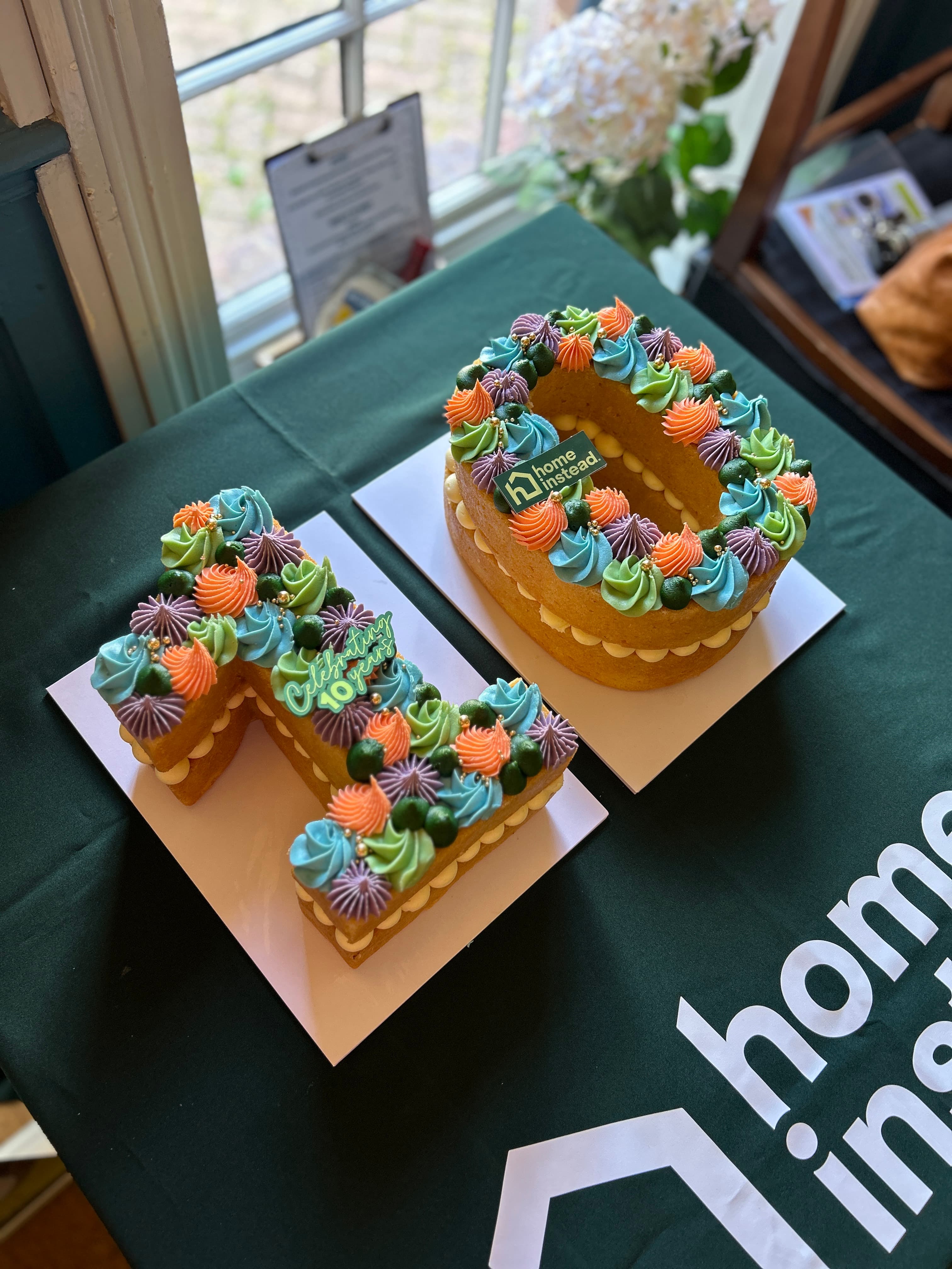 Two colourful number-shaped cakes displaying "10" sit on a Home Instead table, created to celebrate the organisation's 10-year anniversary.