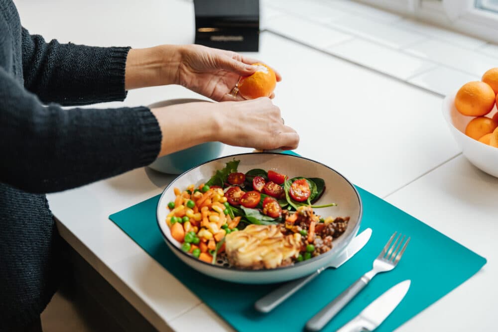 Person preparing a meal with beans, tomatoes, greens, and squeezing an orange at a kitchen worktop. - Home Instead