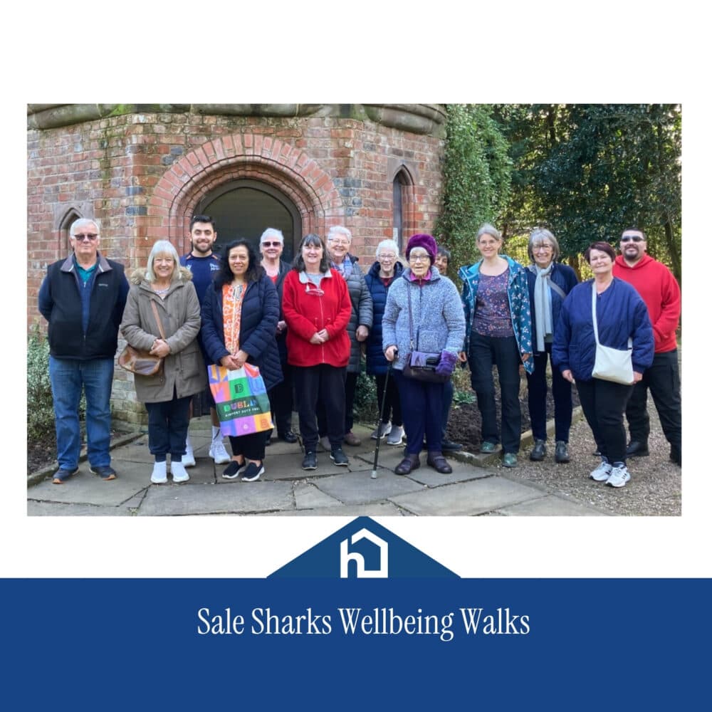 A group of people stands outside a brick building, smiling, for Sale Sharks Wellbeing Walks. - Home Instead