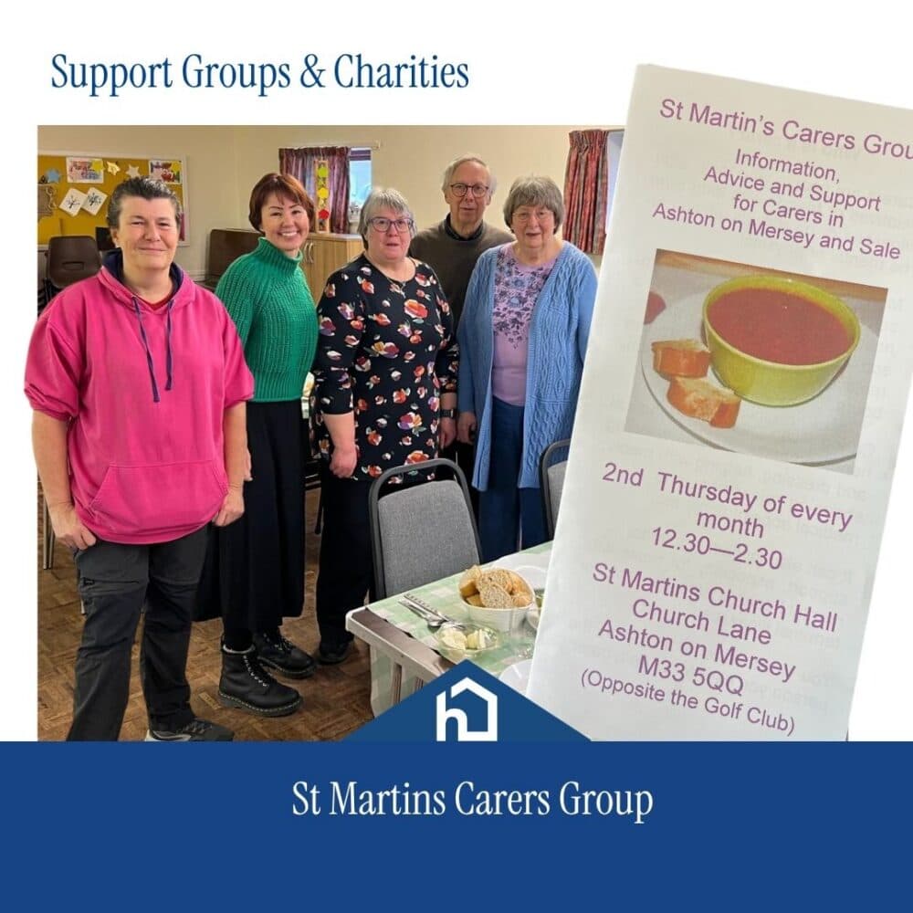 Six people stand smiling next to a leaflet for St Martin’s Carers Group support meeting at a church hall. - Home Instead