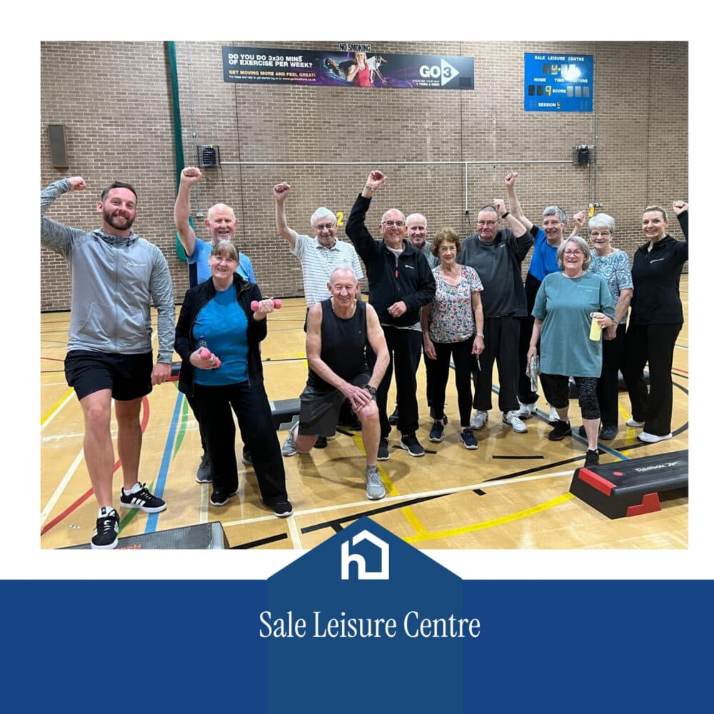 A group of active pensioners poses and smiles in a gym at Sale Leisure Centre, raising their arms in celebration. - Home Instead