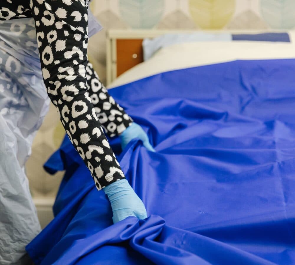 A woman wearing blue gloves fixing the bed