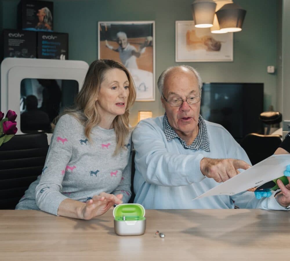An older man and woman sit at a table, looking at papers together in a cosy, well-lit room. - Home Instead