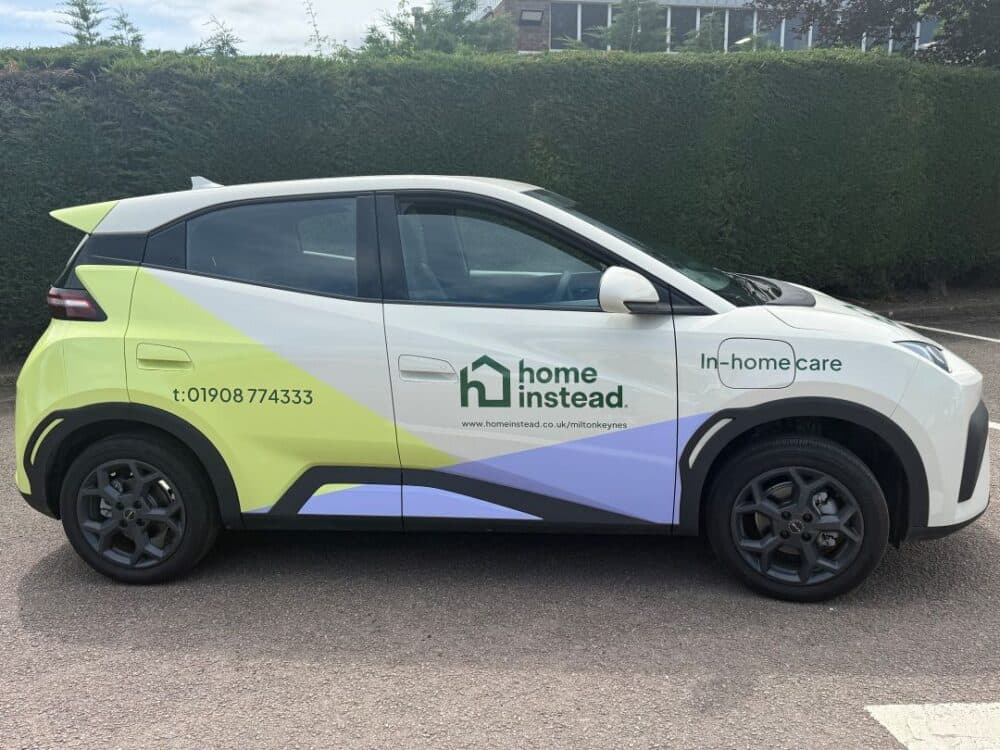 A car with "home instead In-home care" branding and contact details parked on a road. - Home Instead