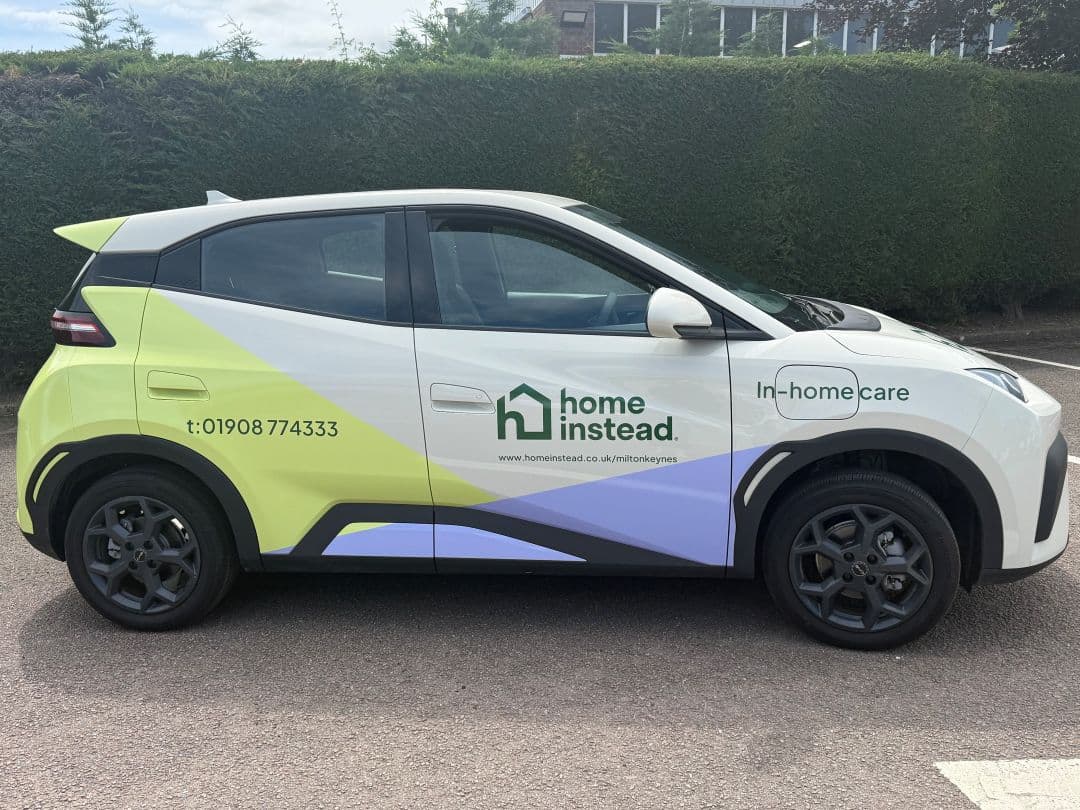 A car with "home instead In-home care" branding and contact details parked on a road. - Home Instead