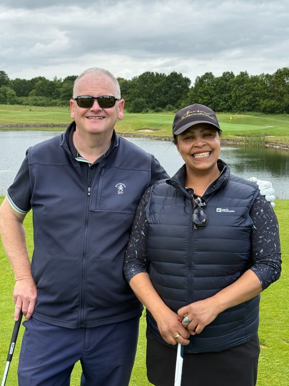 two smiling people wearing sunglasses on a golf course - Home Instead