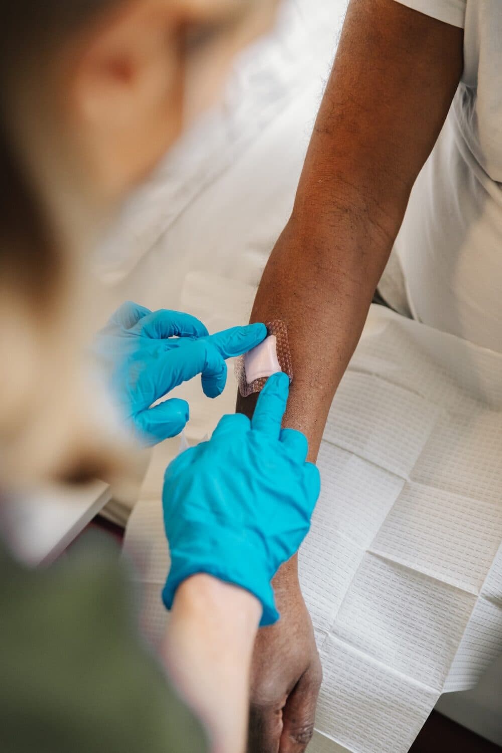 A person in blue gloves places a plaster on another person's forearm after a procedure. - Home Instead